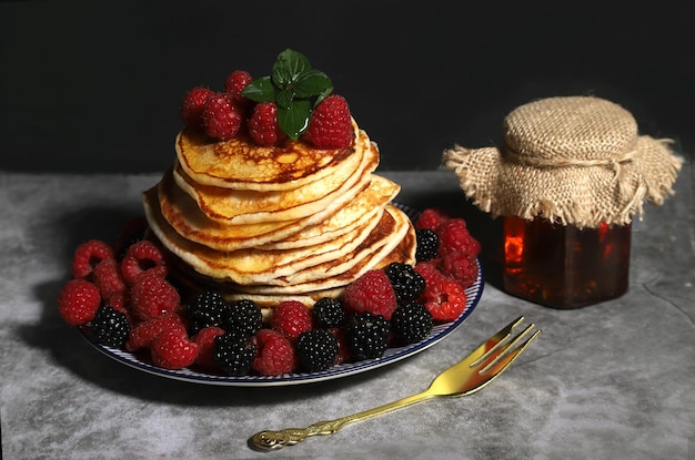 Un montón de tortitas caseras en un plato con frambuesas y moras