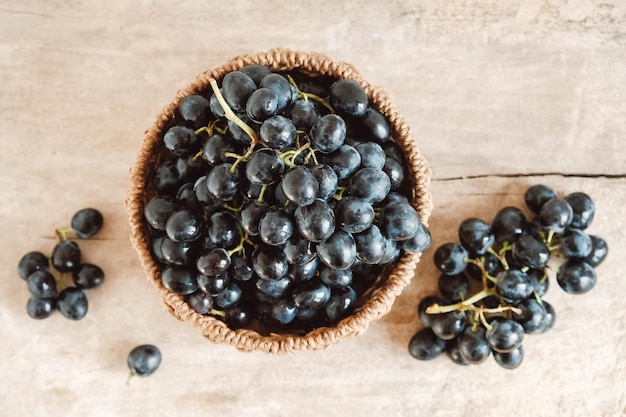 Montón de uvas negras en una cesta de mimbre redonda sobre una mesa de madera antigua