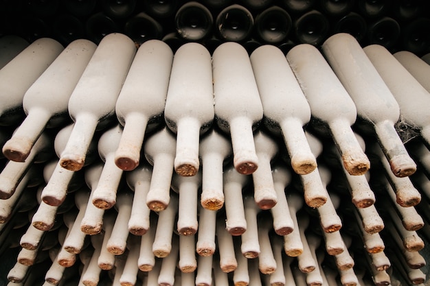 Un montón de viejas botellas de vino cubiertas de polvo descansando botellas de vino apiladas en estantes de madera en el sótano