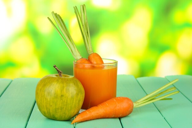 Foto montón de zanahorias y vaso de jugo de manzana verde sobre una mesa de madera de color sobre fondo brillante