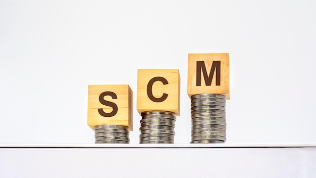 Montones de monedas en aumento con las letras SCM en los cubos de madera fondo blanco concepto de negocios y finanzas