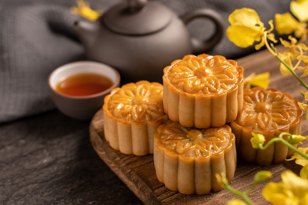 Mooncake, pastel de luna para el Festival del Medio Otoño, concepto de comida festiva tradicional en la mesa de pizarra negra con té y flor amarilla, de cerca, copie el espacio.