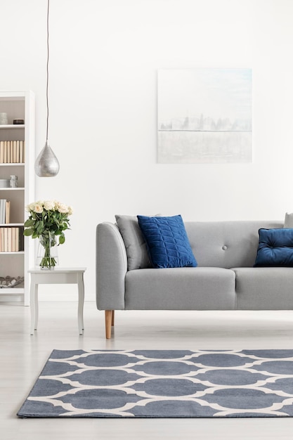 Foto moqueta estampada frente a un sofá gris con almohadas azules en un interior de loft blanco con flores foto real