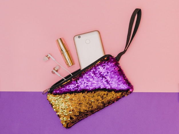 Morado con bolso dorado para mujer con teléfono y lápiz labial en una mesa de dos colores