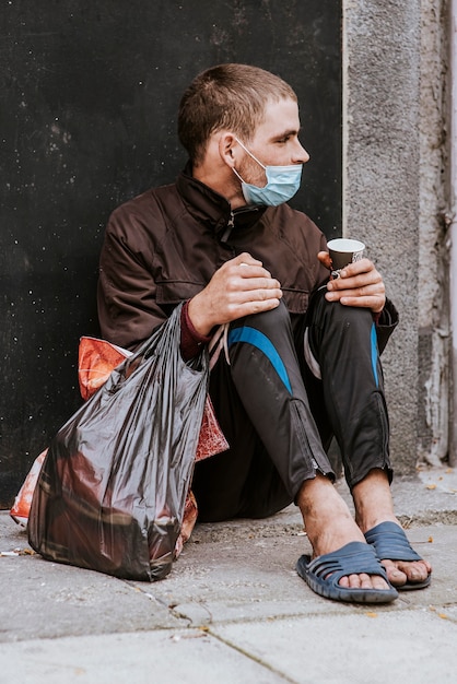 Foto morador de rua com máscara médica ao ar livre e sacola plástica