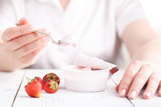 Morango com creme de leite na mesa branca com colher na mão feminina