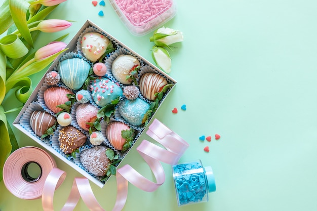 Morangos cobertos de chocolate artesanais, flores e decoração para cozinhar a sobremesa sobre fundo verde, com espaço livre para texto