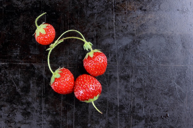 Morangos doces suculentos vermelhos com galhos em um fundo preto Closeup de frutas vermelhas Conceito de comida saudável