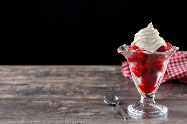 Morangos e chantilly em copo de sorvete na mesa de madeira