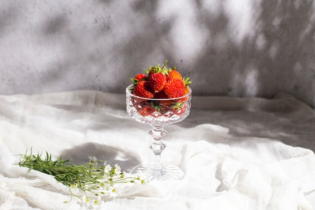 Morangos frescos e suculentos em um copo, um buquê de flores silvestres em uma mesa sobre um fundo de concreto.