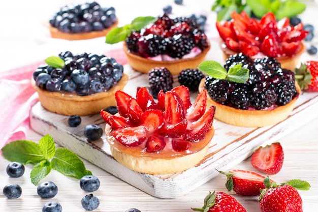 Morangos, mirtilos, tortinhas de amoras com ganache de chocolate, frutas frescas e folhas de hortelã, foco seletivo. Torta de frutas frescas, bolo de frutas feito na hora em uma mesa