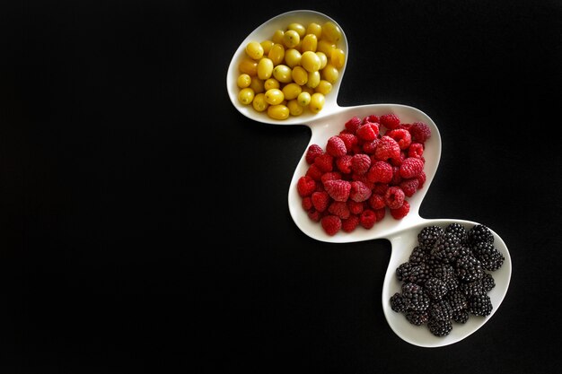 moras y dogeberry en plato blanco sobre fondo negro