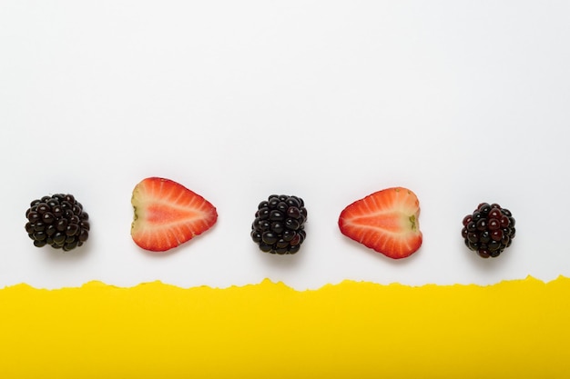 Foto moras y fresas cortadas sobre fondo amarillo con borde de papel blanco rasgado