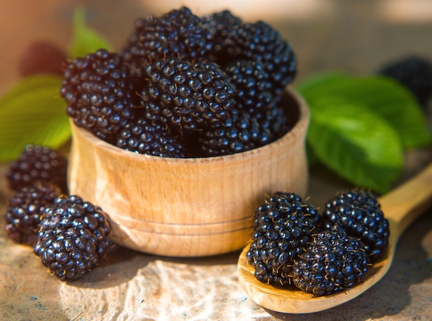 Moras frescas en un cuenco y una cuchara de madera en una tabla vieja