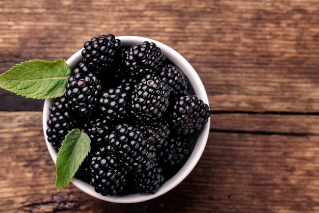 Moras en un recipiente blanco con hojas de menta sobre un fondo de madera de cerca.