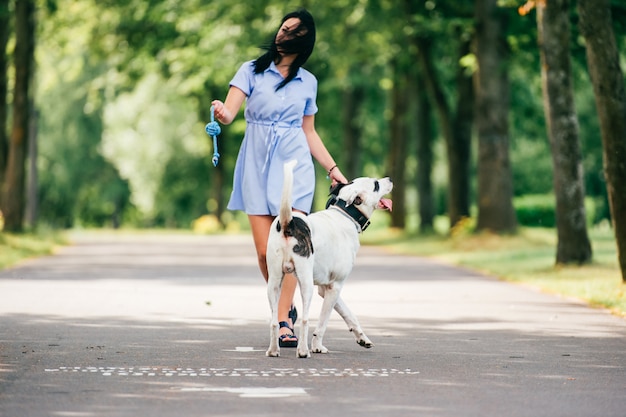 Foto morena alegre brincando com seu cachorro branco no parque de verão