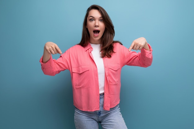 Una morena alegre con una camisa rosa y jeans señala con el dedo la información en un estudio