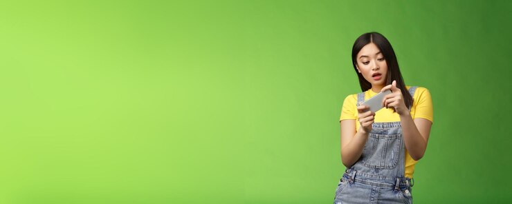 Foto morena asiática fofa nerd despreocupada perde tempo campus universitário jogando olhar de jogo de smartphone online