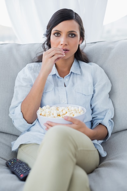 Morena bonita concentrada viendo televisión y comiendo palomitas de maíz