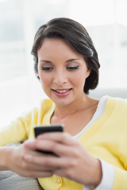 Foto morena casual concentrada en mensajes de texto de cardigan amarillo con su teléfono móvil