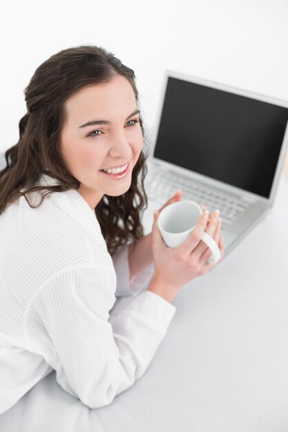 Morena casual con taza de café y portátil en la cama