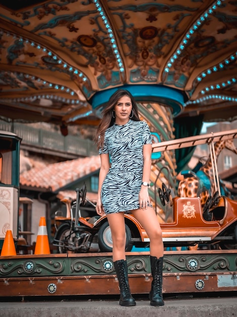 Morena caucasiana sexy de estilo de rua em um carrossel na feira com saia curta