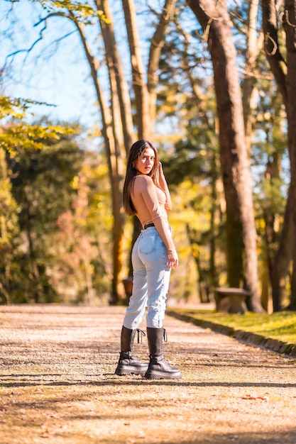 Morena caucásica joven en un suéter rosa y jeans caminando en un parque en otoño