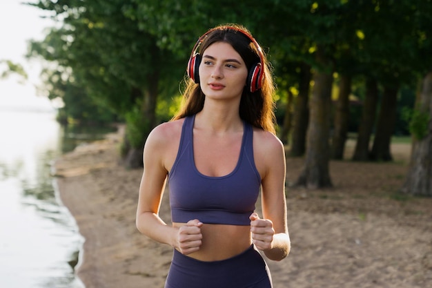 Una morena con chándal corre por la playa con auriculares Entrenamiento matutino en verano