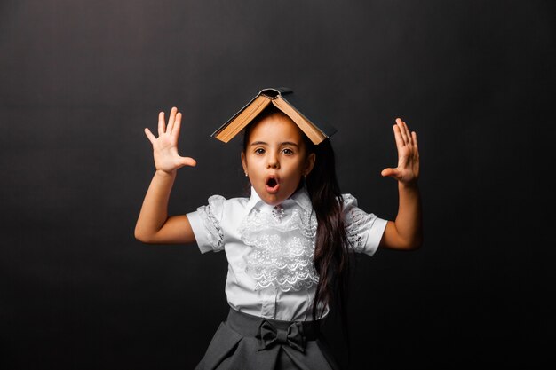 Morena colegial com um livro na cabeça levantando emocionalmente as mãos