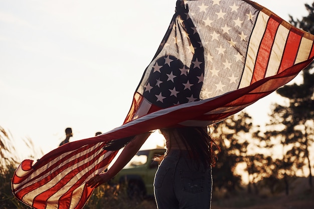 Morena com a bandeira dos eua nas mãos se diverte e sente liberdade ao ar livre em dia de sol