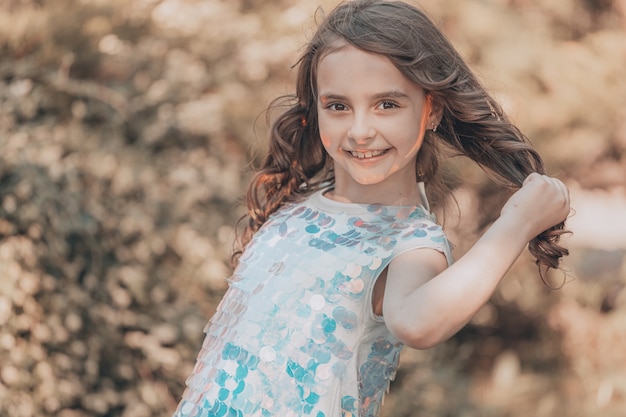 Morena da menina criança com cabelos escuros em um vestido brilhante na natureza. tingimento de baunilha. Foto de alta qualidade