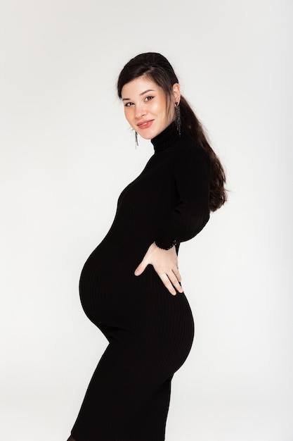 Morena embarazada con un vestido negro con cuello en un fondo gris