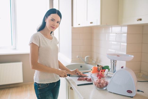 Morena se encuentra en la cocina. Ella corta la carne en trozos. Mujer cocina comida.