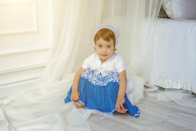 Morena engraçada e fofa menina sorridente brincando e sentado relaxando no quarto branco claro em casa. interior branco com cama grande. infância, pré-escola, juventude, conceito de relaxamento