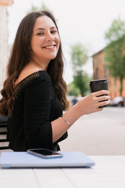 La morena está sentada en un café de verano y tomando café La computadora portátil está sobre la mesa Descanso en el trabajo