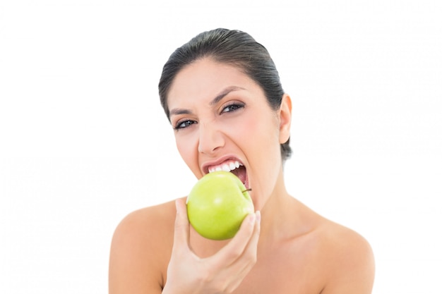 Morena feliz comiendo una manzana verde y mirando a la cámara
