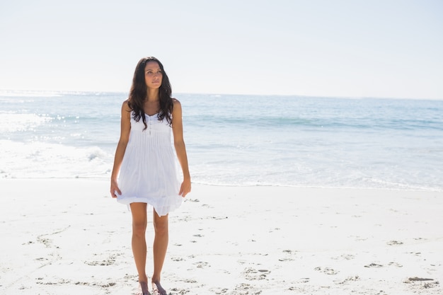 Morena feliz em vestido de sol branco andando na areia