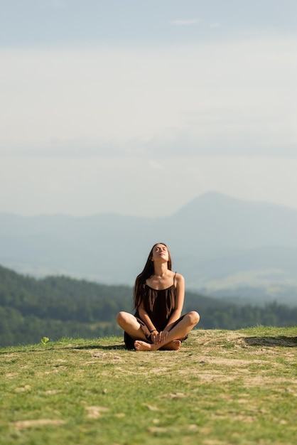 Morena feminina sentada em pose de lótus nas montanhas e meditando nas montanhas