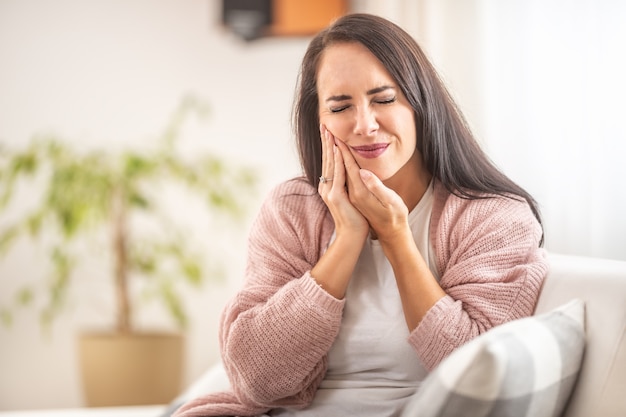 Morena fica em casa com dor de dente, segurando a bochecha direita com as mãos.