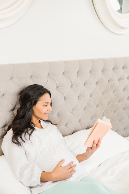 Morena grávida, lendo um livro na cama