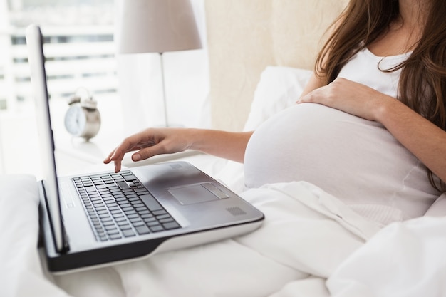 Morena grávida usando laptop na cama