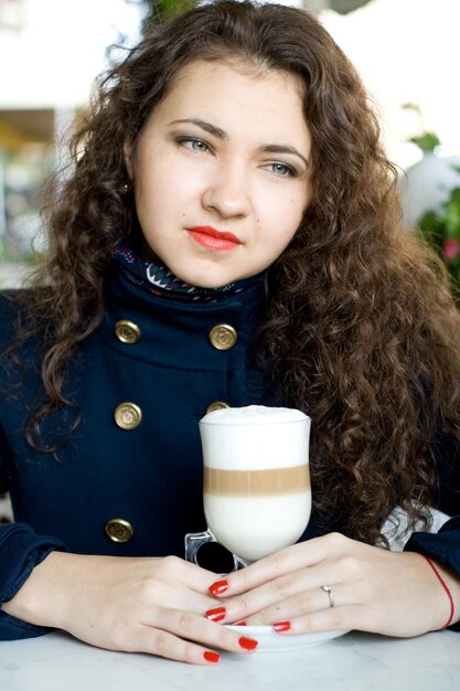 Morena hermosa joven con un delicioso café con leche en un café de la calle