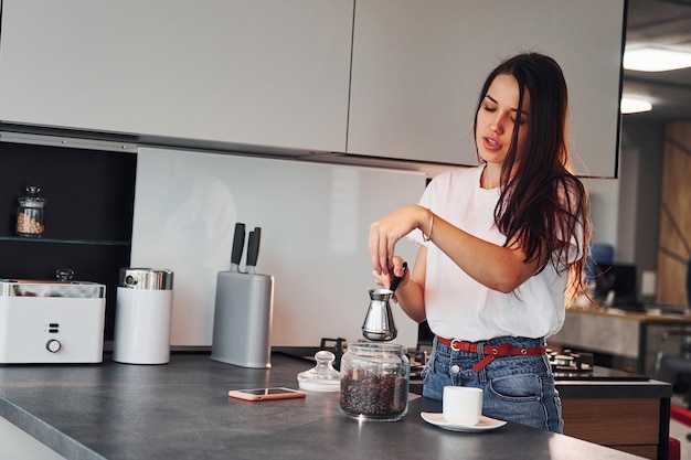 Morena hermosa joven en ropa casual preparando café en la cocina durante el día