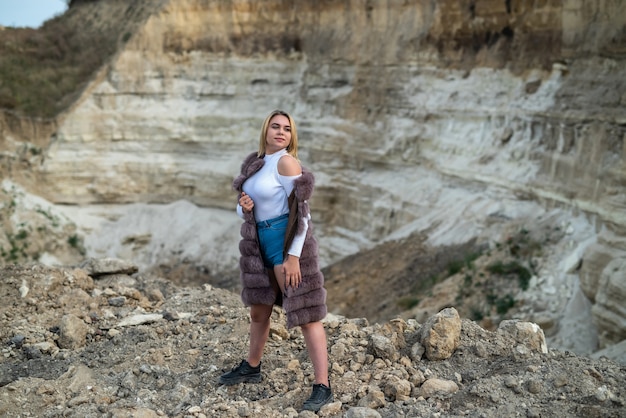 Morena hermosa mujer en abrigo de piel de ocer camiseta y pantalones cortos posando en rocas de arena vacías