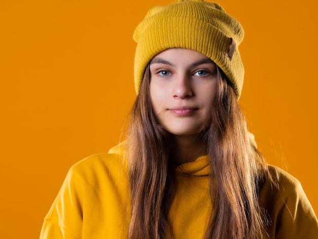 Morena jovem e elegante, alegre, com um moletom amarelo e um chapéu sobre um fundo amarelo