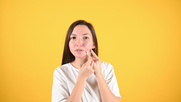 Morena joven que revisa su piel sobre fondo amarillo Cosmetología cuidado de la piel tratamiento del acné Foto de alta calidad