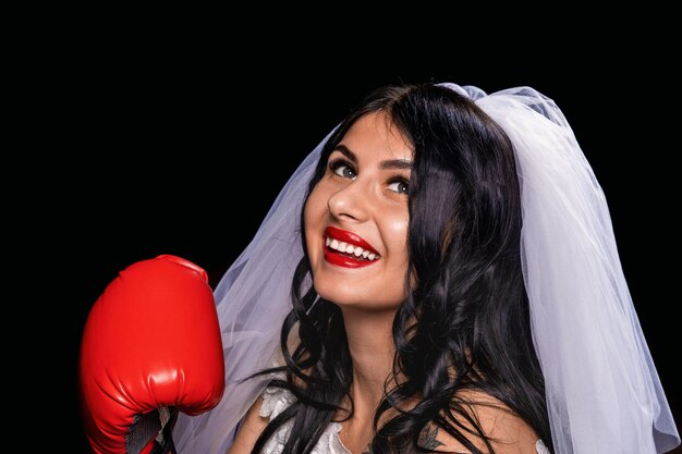 Foto morena con lápiz labial rojo en velo de novia y guantes de boxeo