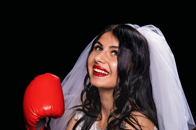 morena con lápiz labial rojo en velo de novia y guantes de boxeo