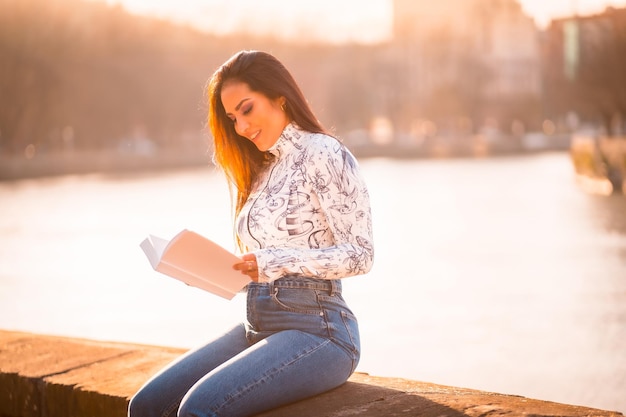 Una morena latina en la ciudad al atardecer junto al río con el sol al fondo