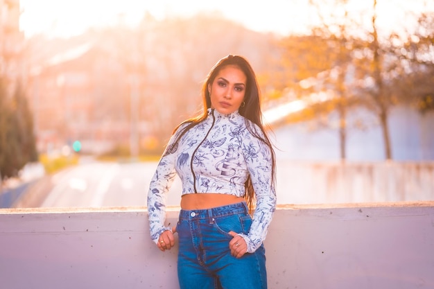 Una morena latina junto a una carretera en la ciudad junto a un árbol con flores rosas al atardecer